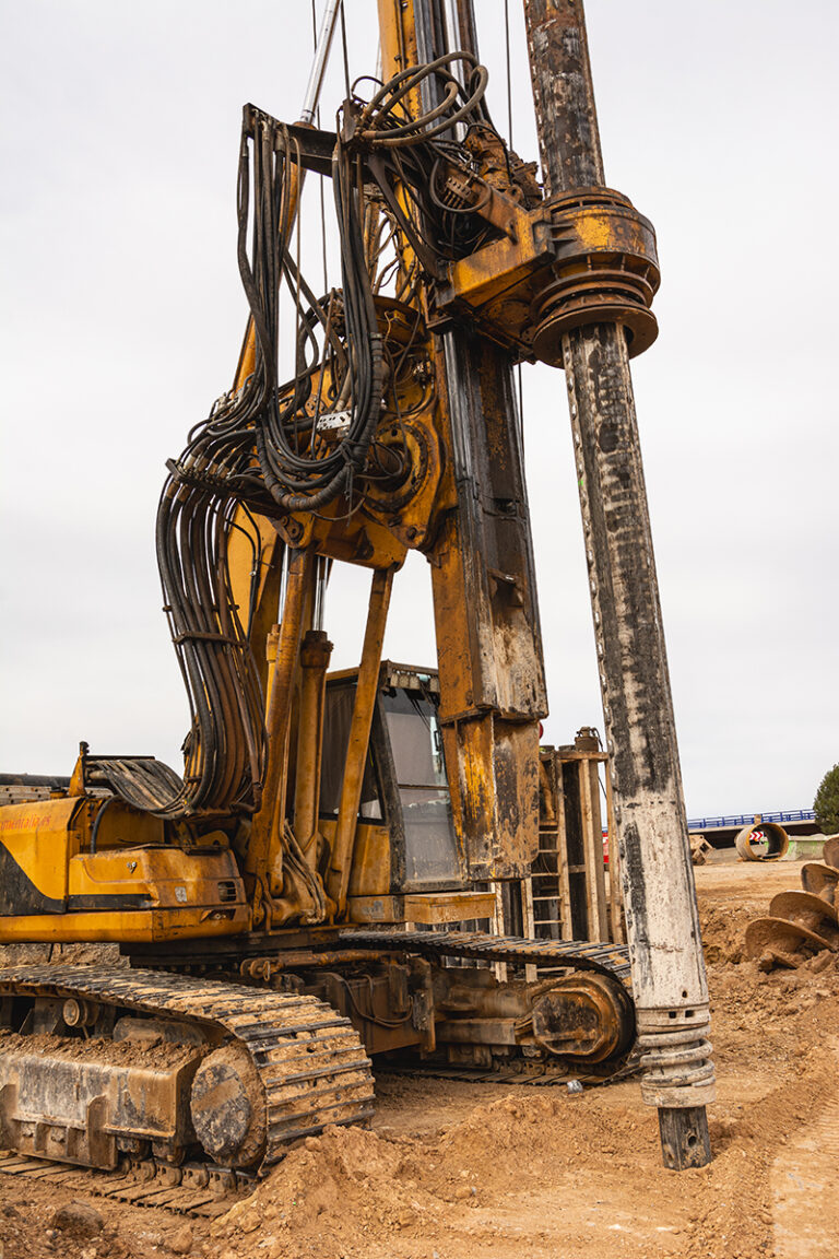 A massive yellow drilling machine operates amidst rocky terrain and sandy surroundings