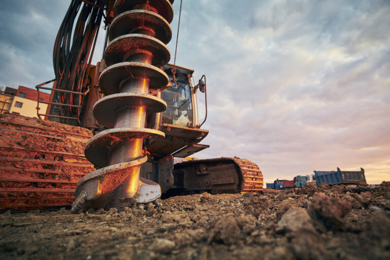 Building activity on contruction site. Close-up view of drilling machine against trucks.